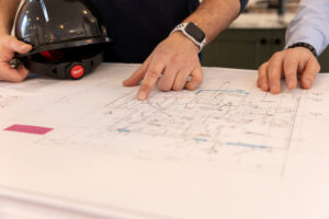OUR BLOGS Two people reviewing architectural drawings on a desk as part of the property development and custom home planning process.